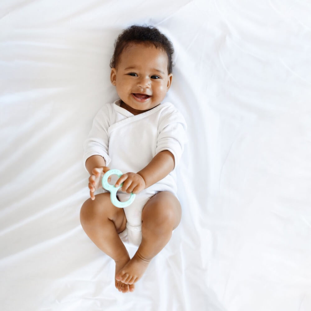 Baby laughing and holding baby teether in hands.