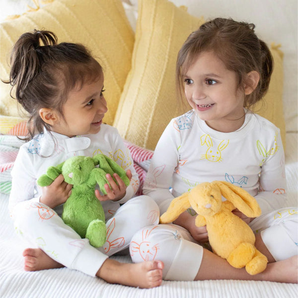 Two young girls playing with plush toys in bed.