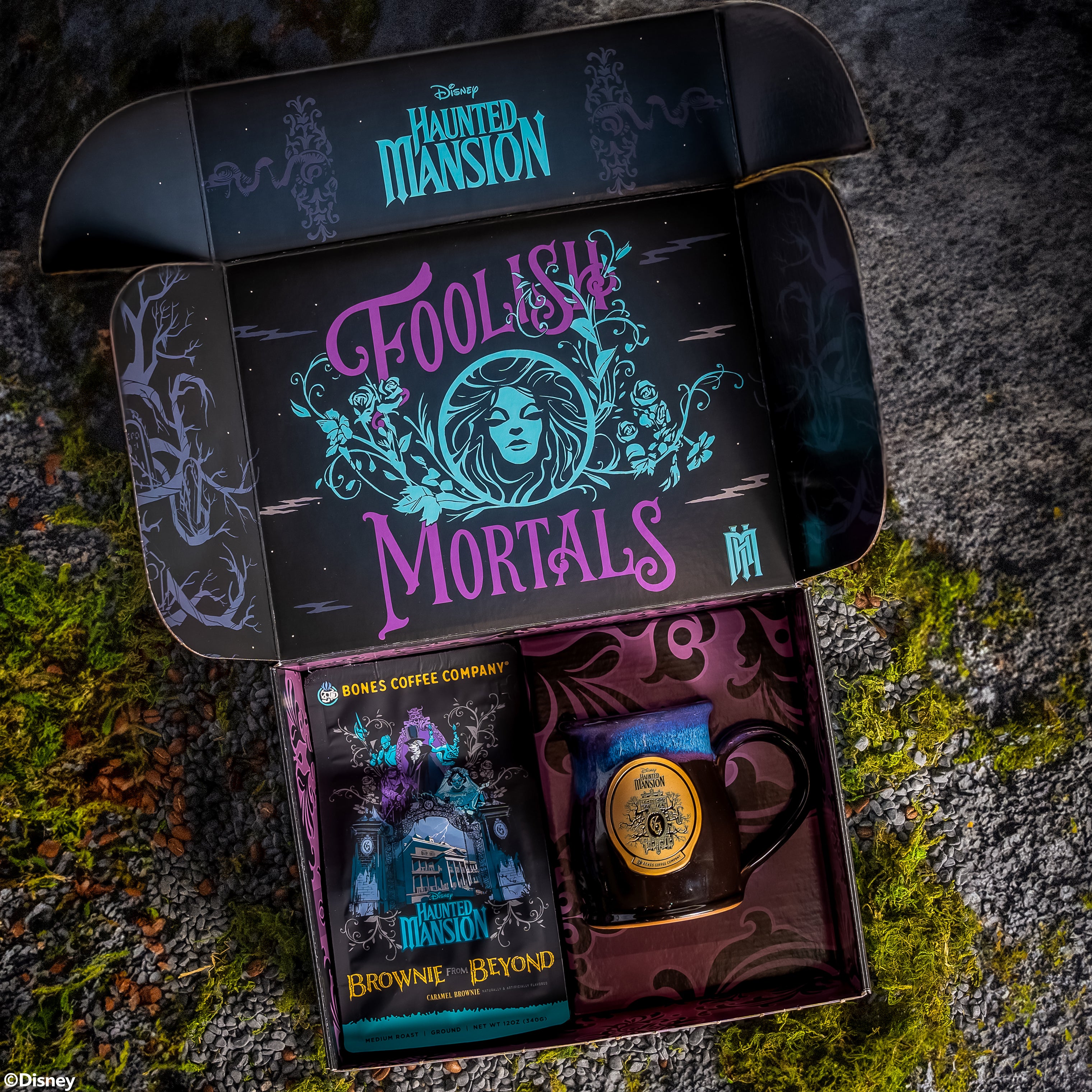 The opened collector's box inspired by Disney Haunted Mansion. It contains a black mug with a white glaze on top of it and a 12 ounce bag of caramel brownie flavored coffee named Brownie From Beyond. The top of the box says Foolish Mortals.