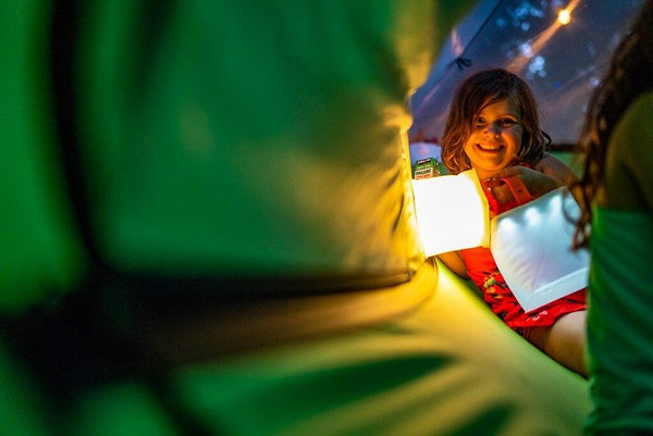 Child in tent with LuminAID light, smiling. Source: Cam McLeod