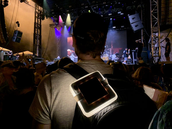 Man with luminaid lantern on his backpack in crowd.