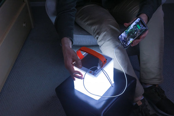 Man charging phone with portable LuminAID power lantern. 