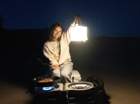 Woman with luminaid lantern cooking dinner at night while camping.