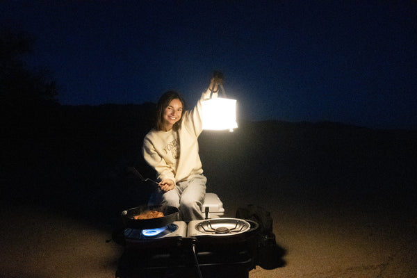 Happy camper cooking over stove holding LuminAID Lantern. Source: Ira Waldman