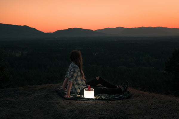 Person sitting on a ledge watching the sunset with a LuminAID Lantern. Source: Richard Kelly