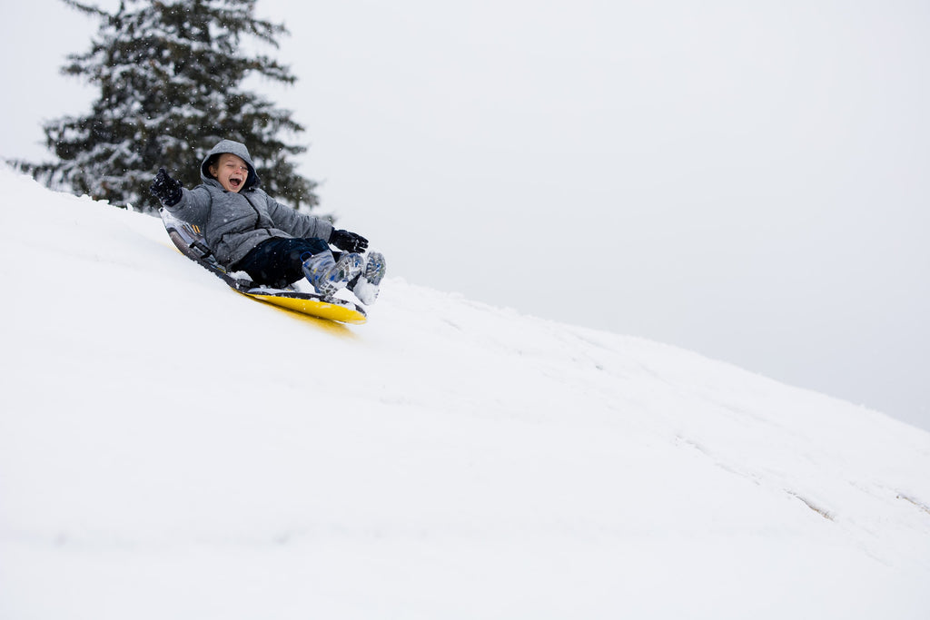Boy sledding down hill in snow.