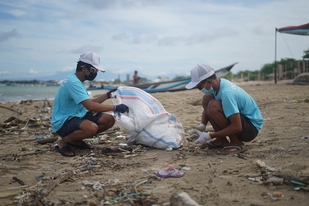 Two people cleaning up trash on the beach near water.