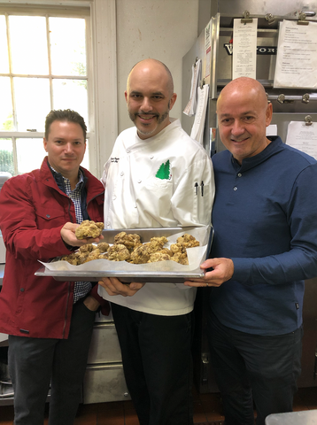 Chef Michael Ruggiero and others in a kitchen holding white truffle on a tray