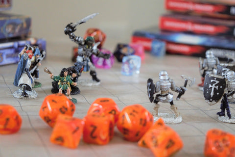 A game of Dungeons & Dragons being played, with orange dice and painted metal miniatures on a vinyl battle mat.