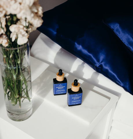 Navy silk pillowcases and facial oil with fresh flowers on bedside table