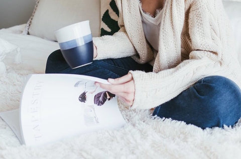 Lady in knit cardigan sitting on bed reading magazine