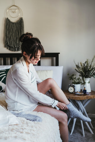 Girl in white pajamas sitting on bed putting on grey socks