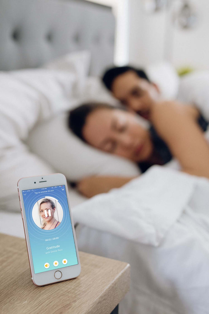 iPhone with app on screen standing on nightstand next to sleeping couple