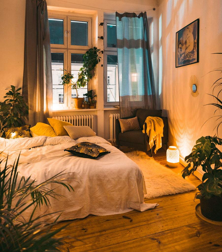 Overview of white bed in warm lighting with plans and yellow accent pillows and blankets.