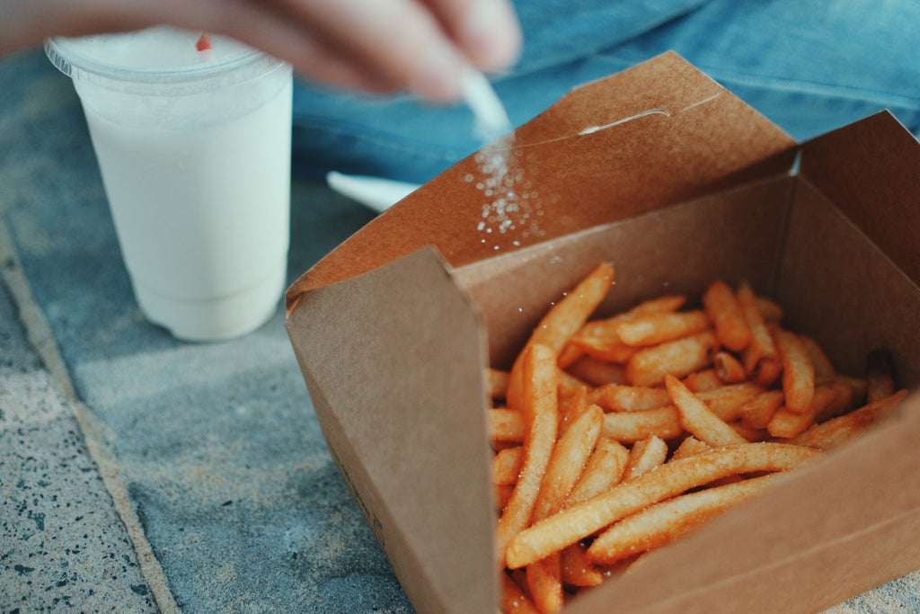 Close up of someone pouring salt on to-go container of fries next to milkshake