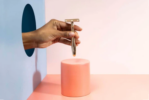 Hand holding a razor over a pink cylinder