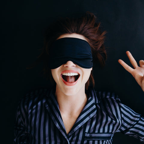 girl smiling and wearing silk blackout eyemask holding up peace sign