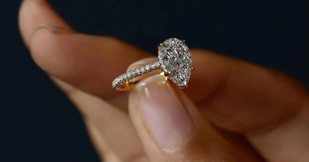 γυναικείο χέρι κρατάει μονόπετρο δαχτυλίδι με διαμάντι από κίτρινο χρυσό σε σχήμα δάκρυ 