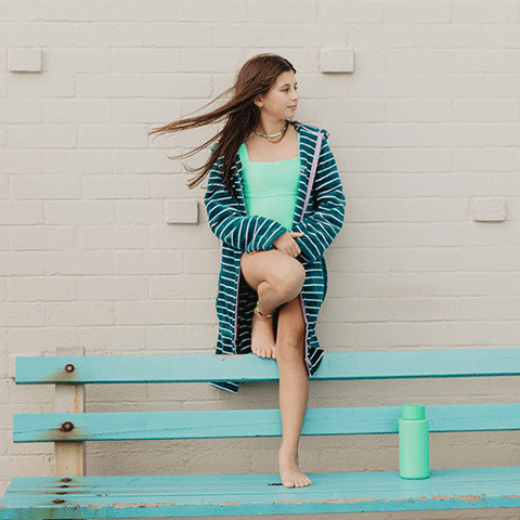 Havana wearing her turquoise swoodi and bright green one piece bahting suit. On the beach and holding a skateboard.