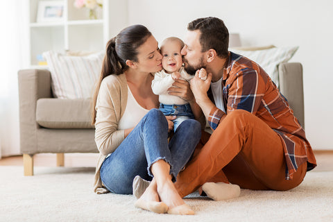 photo of couple holding a baby and kissing the baby on either side of its face.