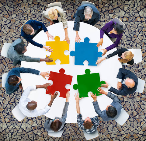 photo of a group of people sitting at a table putting yellow, blue and red puzzle pieces together.