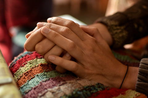 hands clasped together on top of a knitted blanket.