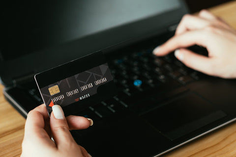 close up photo of a person holding a credit card and typing on a keyboard.