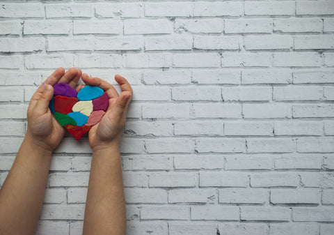 child's hands holding a patchwork heart on a brick wall backdrop.