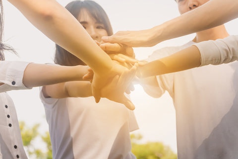 photo of a group of people putting their hands together in a group huddle.