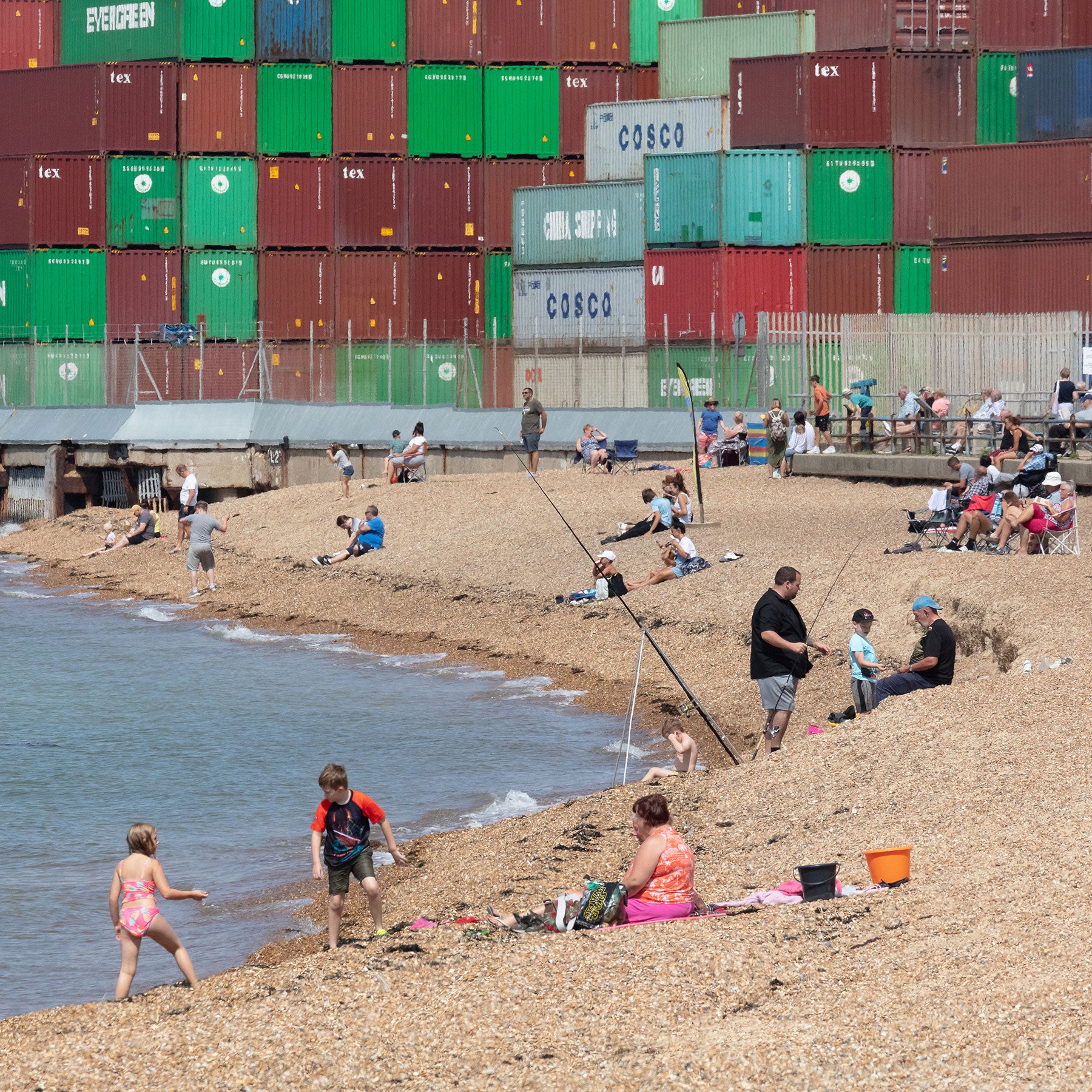 Families on a pebble beach in sight of huge shipping containers