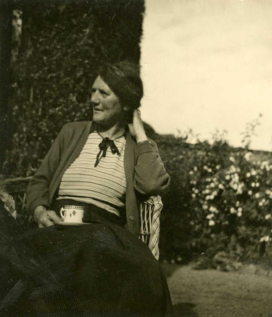 Writer, hill-walker, adventurer and explorer Nan Shepherd sits on a bench with a cup of tea and nature in the background