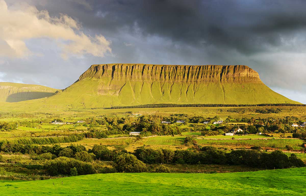 A landscape view of Benbulben mountain with a grey sky and green fields in County Sligo, Ireland.
