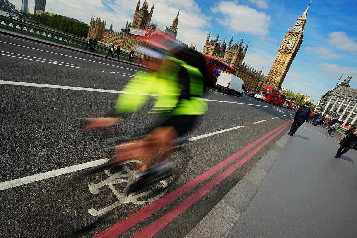 A cyclist commutes on their bike through the busy streets of central London with Big Ben, Westminster and the Houses of Parliament in the background.