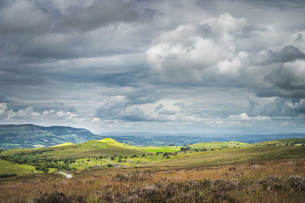Green hills and pastures illuminated by patches of sunlight and stormy sky in Cuilcagh Mountain Park, Fermanagh, Northern Ireland.