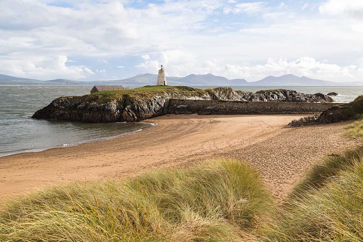 A landscape view of sand dunes, a sandy beach, and Twr Bach lighthouse by the sea in  Anglesey, North Wales, UK.