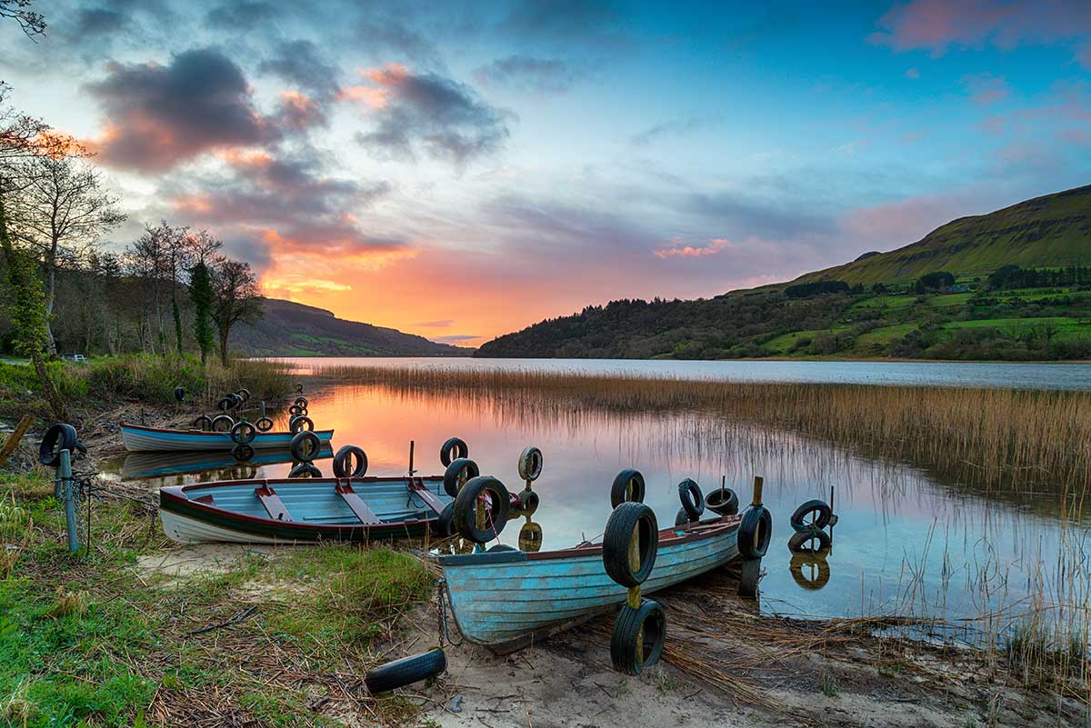 A beautiful sunrise over Glencar Lough in County Sligo, Ireland, with boats and mountains in the background.