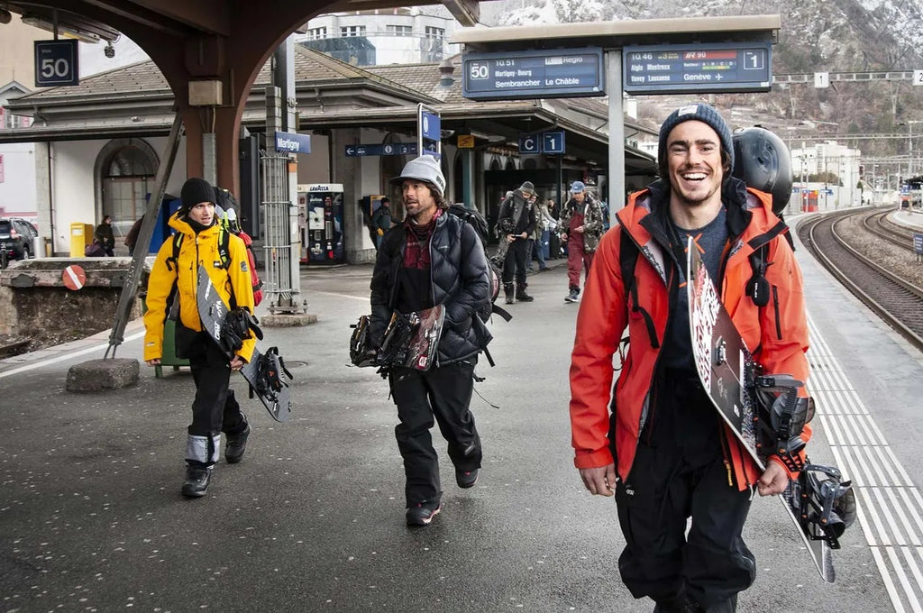 Three snowboarders on a train station platform in the Swiss Alps