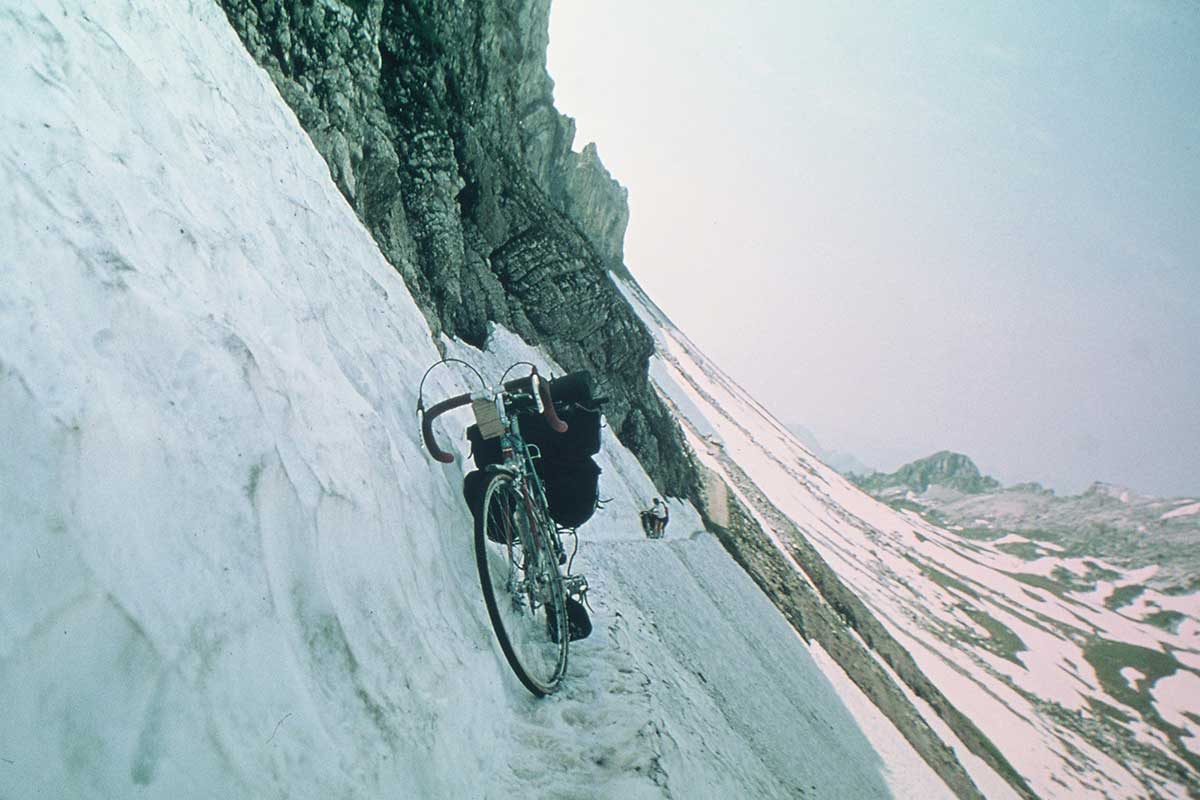 A Rough Stuff Fellowship image of a cycling trip in the snowy mountains on a very steep cliff edge and narrow path.