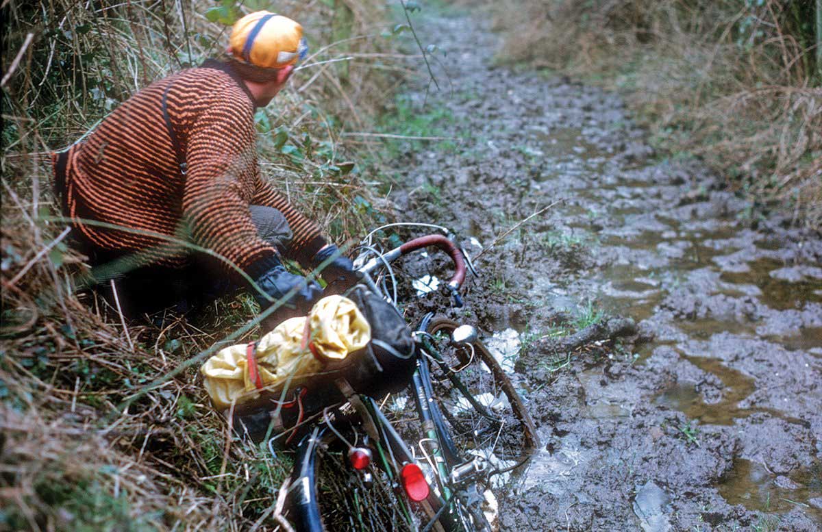 A Rough Stuff Fellowship member with their bicycle on a cycling trip in the countryside on a muddy country path.