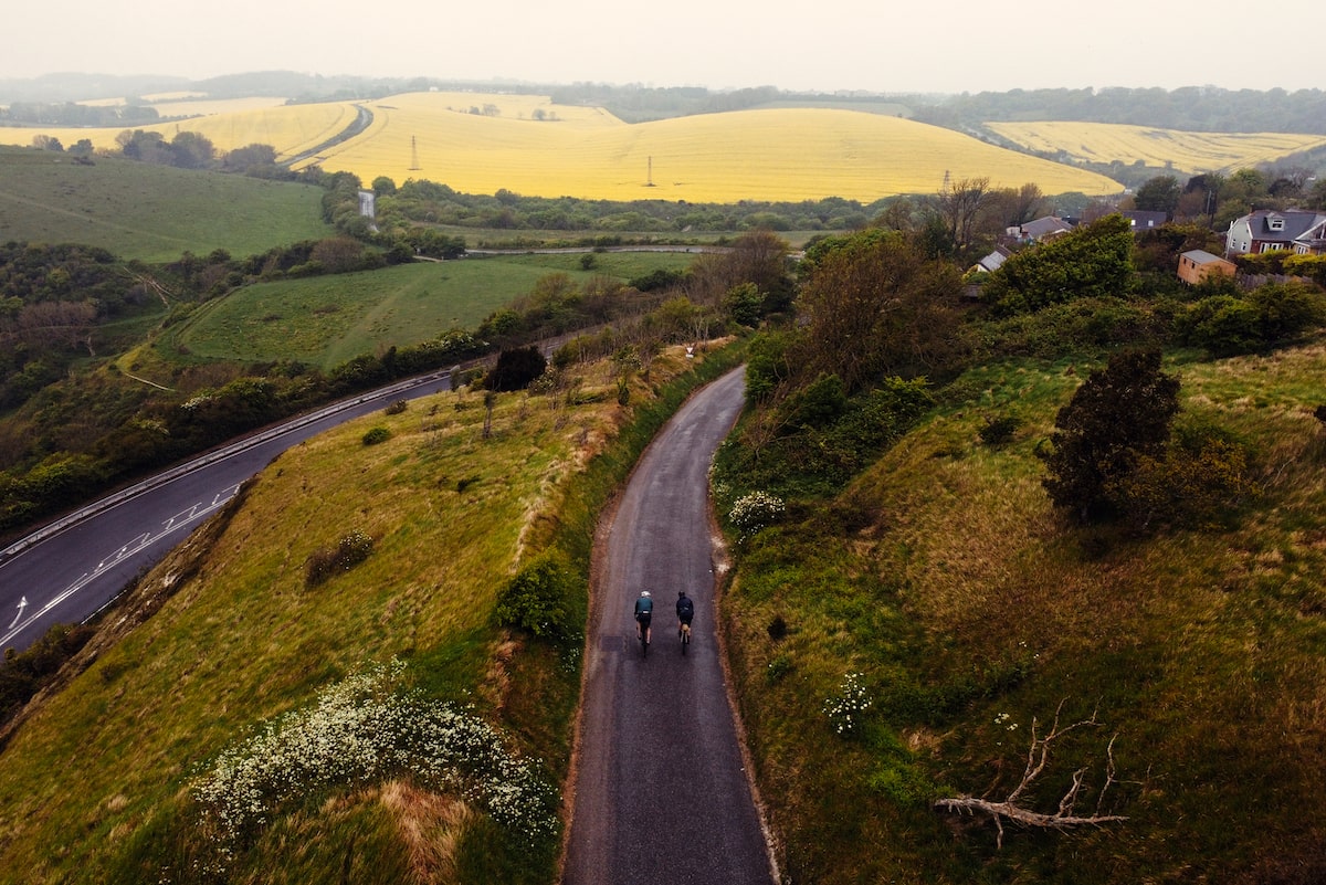 Two cyclists travel along a quiet tarmac road, surrounded by fields, in Kent on a bikepacking trip. Credit: Cycling UK