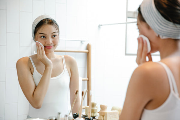 Asian woman applying coconut cider vinegar toner while looking at mirror