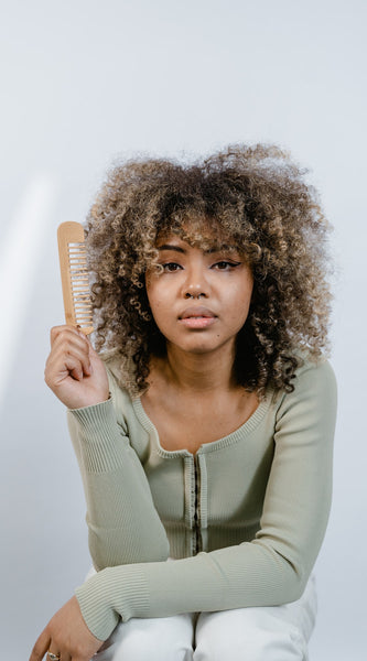 Woman with thick curly hair holding a comb while sitting down