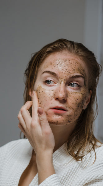 Woman applies an anti-aging herbal scrub to her face, highlighting skincare products for changing seasons and the importance of a seasonal skincare routine.