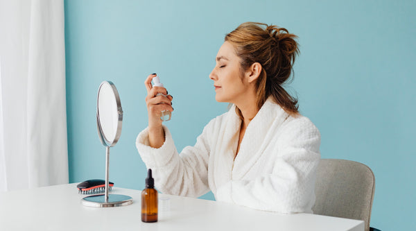 Woman in a white robe sits with her eyes closed while applying spring skincare products and springtime skincare essentials.