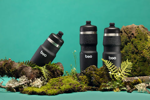 Three Bivo bottles of water in a blue background with moss and other plants