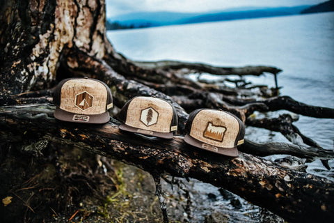 Three Rustek's Cork Hats sitting on a tree root with a lake and mountains as background