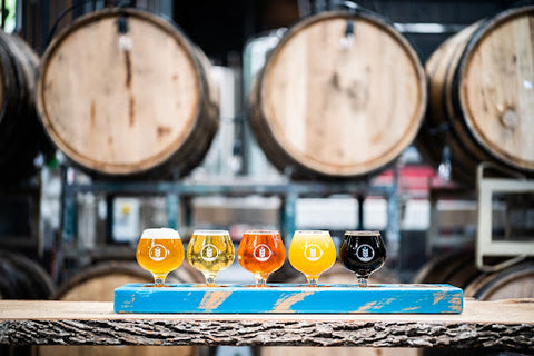 A flight of sustainable beers sitting in front of beer barrels
