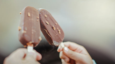 two hands each holding a chocolate covered ice cream bar with nuts on the outside 