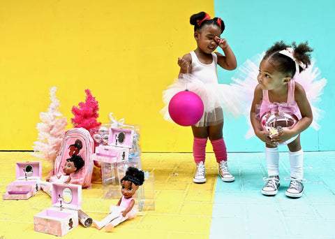 image of two little black girls dressed in tutus in front of Christmas scene with Nia Ballerina black ballerina music box, doll and rucksack