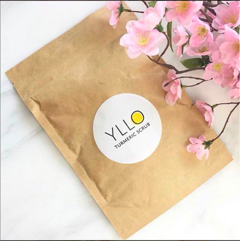 Yllo face scrub packed lying on table with pink flowers.